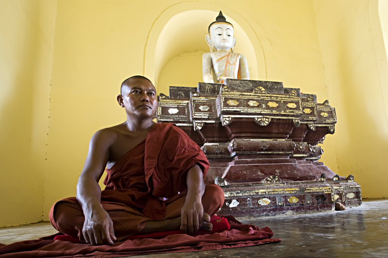 A monk ponders under Buddha's sculpture