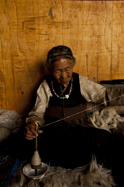 An old Loba women makes wool inside an old house with traditional Tibetan architecture.