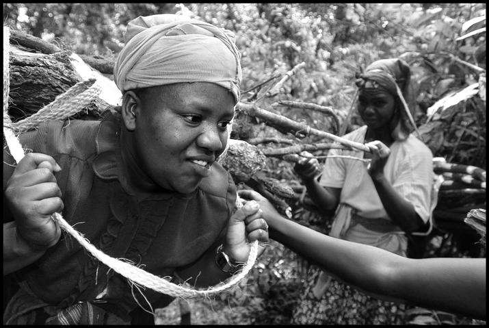 A woman is being helped to load her firewood on her back.